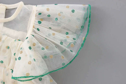 Close-up of white sheer fabric with green and gold polka dots and a green-trimmed ruffle sleeve.