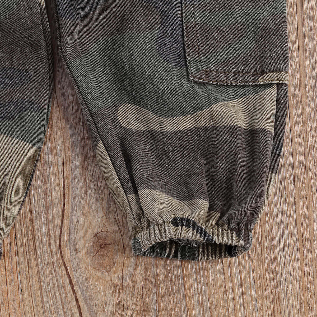 Close-up of camouflage pants cuff with elastic band on wooden background.