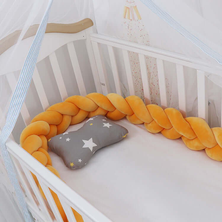 Cozy baby crib with an orange braided bumper and gray star pillow.